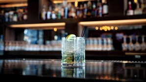 A bar with a glass of iced drink with a lemon slice and straw, and shelves of bottles in the background. - The Landing Hotel at Rivers Casino  (Pittsburgh)