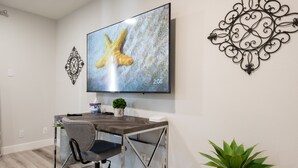 Una habitación moderna con piso de madera, un escritorio con silla, un televisor montado en la pared y decoración en la pared.