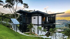 A modern two-story house with a flat roof, large glass windows, and a staircase leading to the upper level. - Odyssey Villa - incredible mountain views, 3 bedrooms, w pool! (Peréz Zeledon)