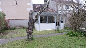 Un edificio con tejado de tejas, un pequeño jardín con césped y un árbol, y un camino que lleva a la entrada.