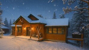 En stuga av trä med ett snötäckt tak, en veranda med skidor och ett snöklätt landskap.