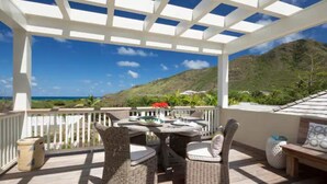 An outdoor patio with wicker furniture, a white pergola, and a view of the ocean and hills. - 2 Villas @ Windswept Residences (Frigate Bay)