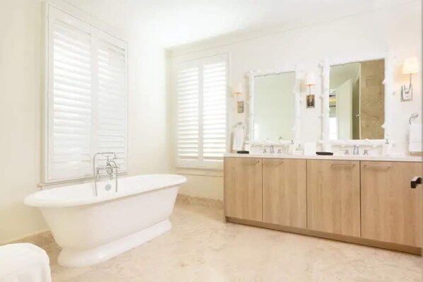 A bathroom with a freestanding bathtub, wooden cabinets, and two large mirrors.