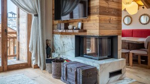 Un salon chaleureux avec une cheminée, des murs en bois, un téléviseur fixé au-dessus de la cheminée et un coin repas avec un canapé rouge.