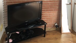 Une pièce avec un mur en briques, un meuble de rangement noir abritant un téléviseur et un meuble blanc.