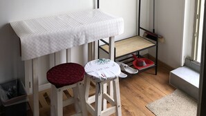 Une petite pièce avec une table blanche, deux tabourets, un présentoir métallique et un balai.