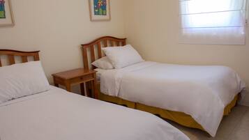 A bedroom with two single beds, a wooden nightstand, and a window with blinds.