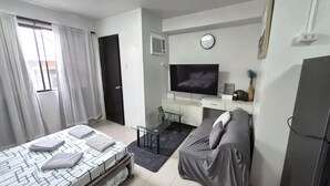Een moderne slaapkamer met een bed, een slaapbank, een televisie en een bureau.