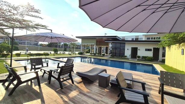 Een zwembadgedeelte met ligbedden en parasols, een houten terras en een modern gebouw op de achtergrond.