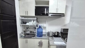 Een kleine keuken met witte kastjes, een magnetron, waterkoker en wasmachine.