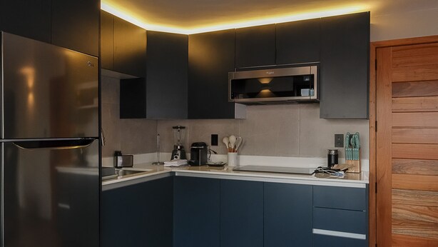 Eine moderne Küche mit dunkelblauen Schränken, einem Edelstahlkühlschrank, einer Mikrowelle und einer Holztür.