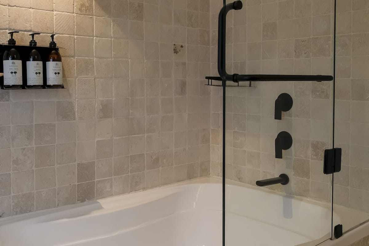 A modern bathroom with a glass-enclosed shower, a white bathtub, and a shelf with three bottles of lotion.