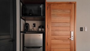Eine kleine Küche mit Kühlschrank, Mikrowelle, Kaffeemaschine und einer Holztür.
