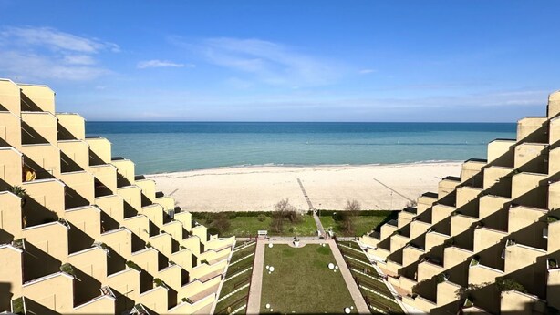 Un hotel frente a la playa con vista al océano, una playa de arena y un césped bien cuidado.