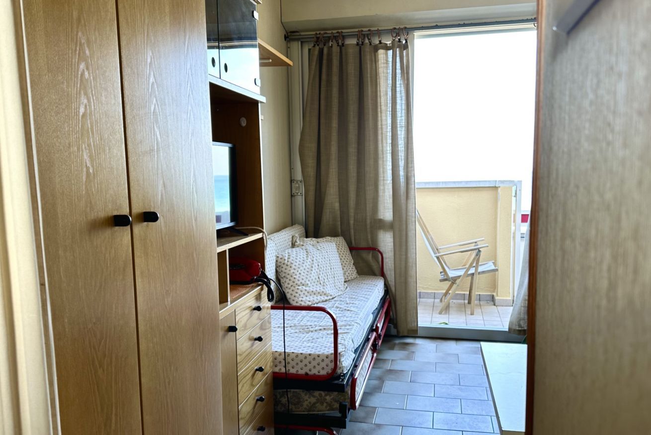 Una habitación con cama, armario y balcón con una silla.