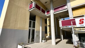Un edificio con letrero de cafetería, mesas al aire libre y puerta de acceso de vidrio.