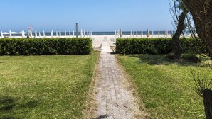 A paved pathway leading to a beach with white umbrellas and a white fence. - SE054 - Senigallia, sea-front studio at the Residence''Pyramids'' (Senigallia)
