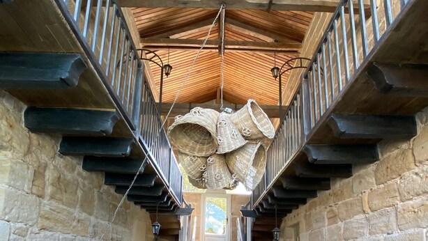 A stone-walled interior with a wooden staircase, wicker furniture, and a hanging basket.