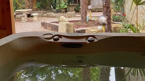 A hot tub with a view of a garden area featuring palm trees, decorative lanterns, and outdoor furniture.