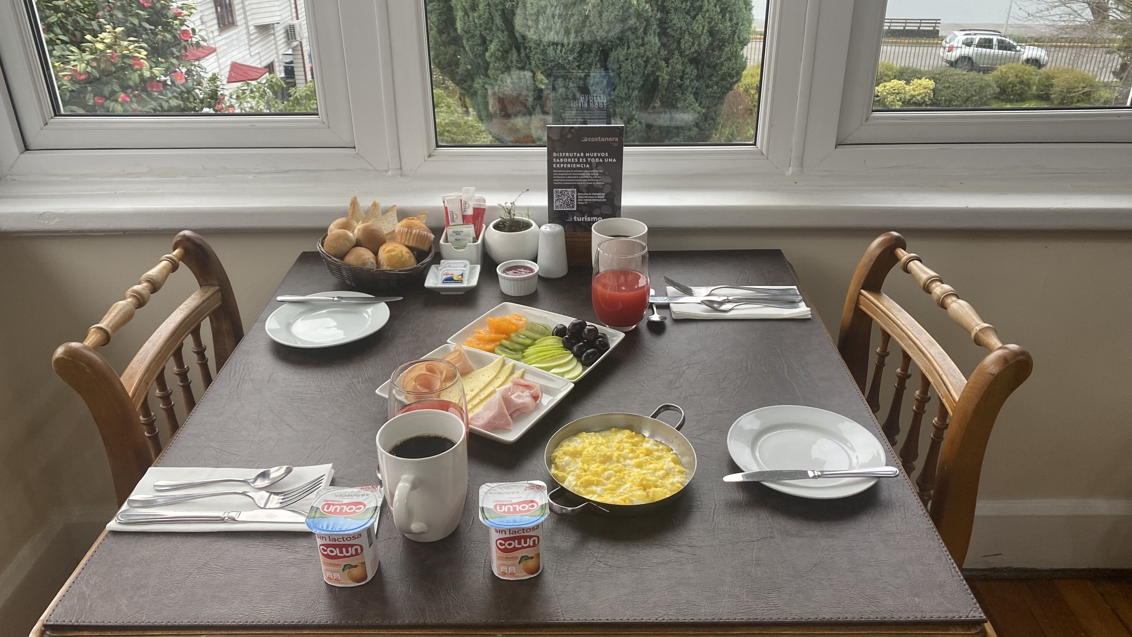 A breakfast table with various food items, a glass of juice, and a sign about a new experience.