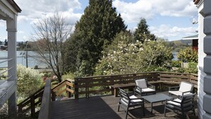 Een houten terras met buitenmeubilair, uitzicht op een meer en een grote altijdgroene boom.