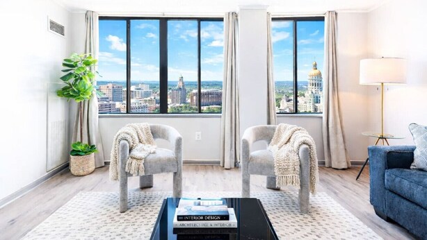 Un salon moderne avec deux fauteuils, une table basse et une vue sur le paysage urbain, visible à travers de grandes fenêtres.