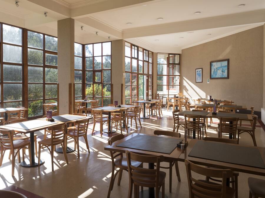 A spacious dining area with large windows, wooden tables and chairs, and framed artwork on the walls.