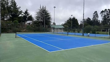 A tennis court with a net, surrounded by a fence and trees.