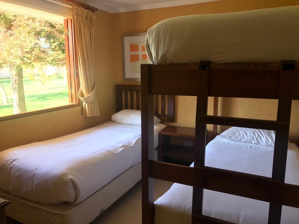 Une chambre avec deux lits superposés, une fenêtre avec des rideaux, un tableau encadré au mur et une petite table de chevet.
