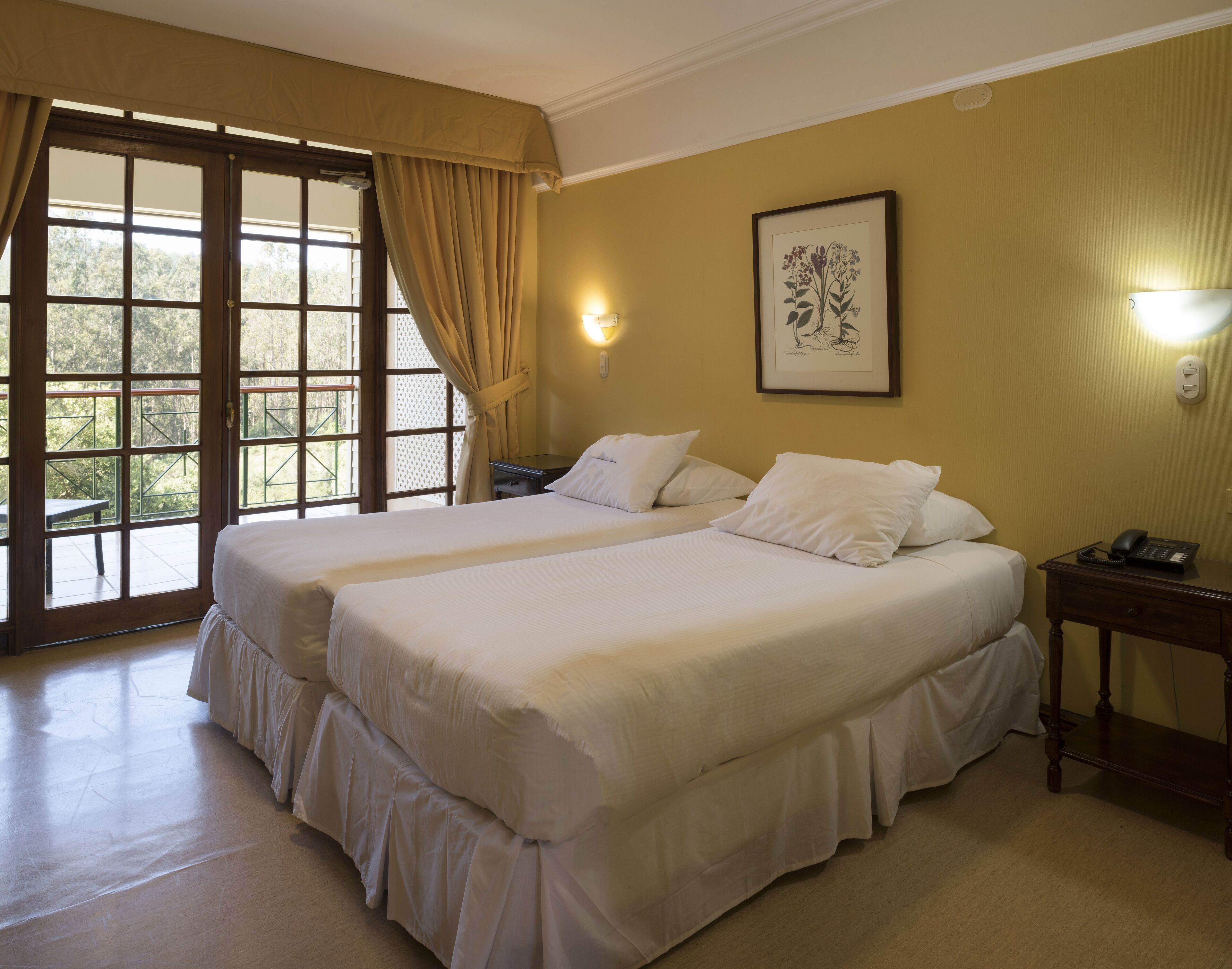 Habitación de hotel con dos camas, un ventanal con cortinas, una obra de arte enmarcada en la pared y una mesita de noche con un teléfono.
