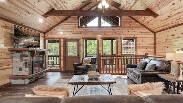 A cozy cabin interior with a stone fireplace, leather sofas, and a wooden deck.