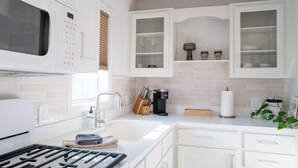 A modern kitchen with white cabinetry, a built-in microwave, a sink, and a coffee maker.