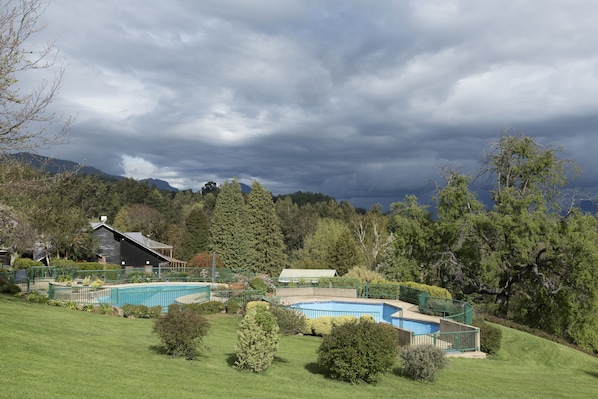 A residential area with a swimming pool, green lawns, and a house with a dark roof.