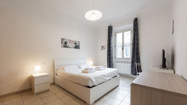 A modern bedroom with a bed, bedside tables, a desk, and a window with curtains. - Mosse 82 apartment in Florence by Mmega (Firenze)