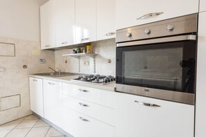 Una cucina moderna con mobili bianchi, piano cottura a gas, forno e una schiena di acciaio inossidabile.