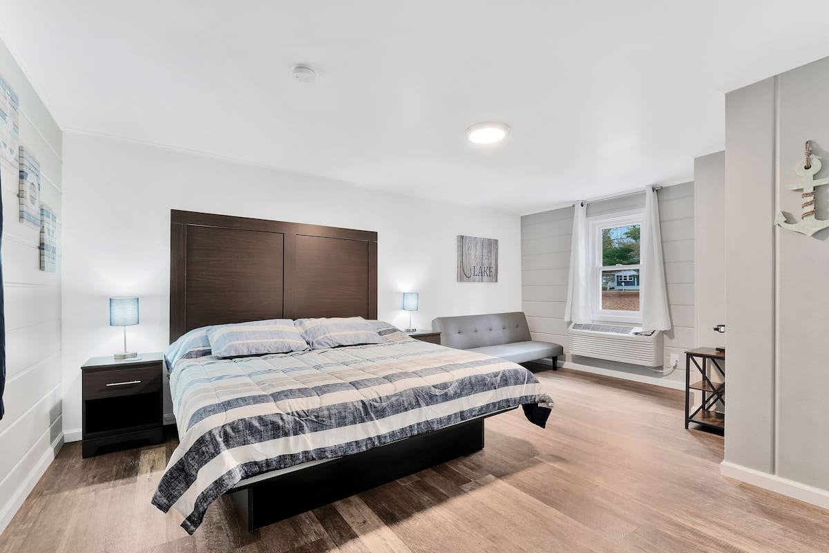 Un dormitorio con una cama grande, mesitas de noche, un sofá gris y una ventana con cortinas.