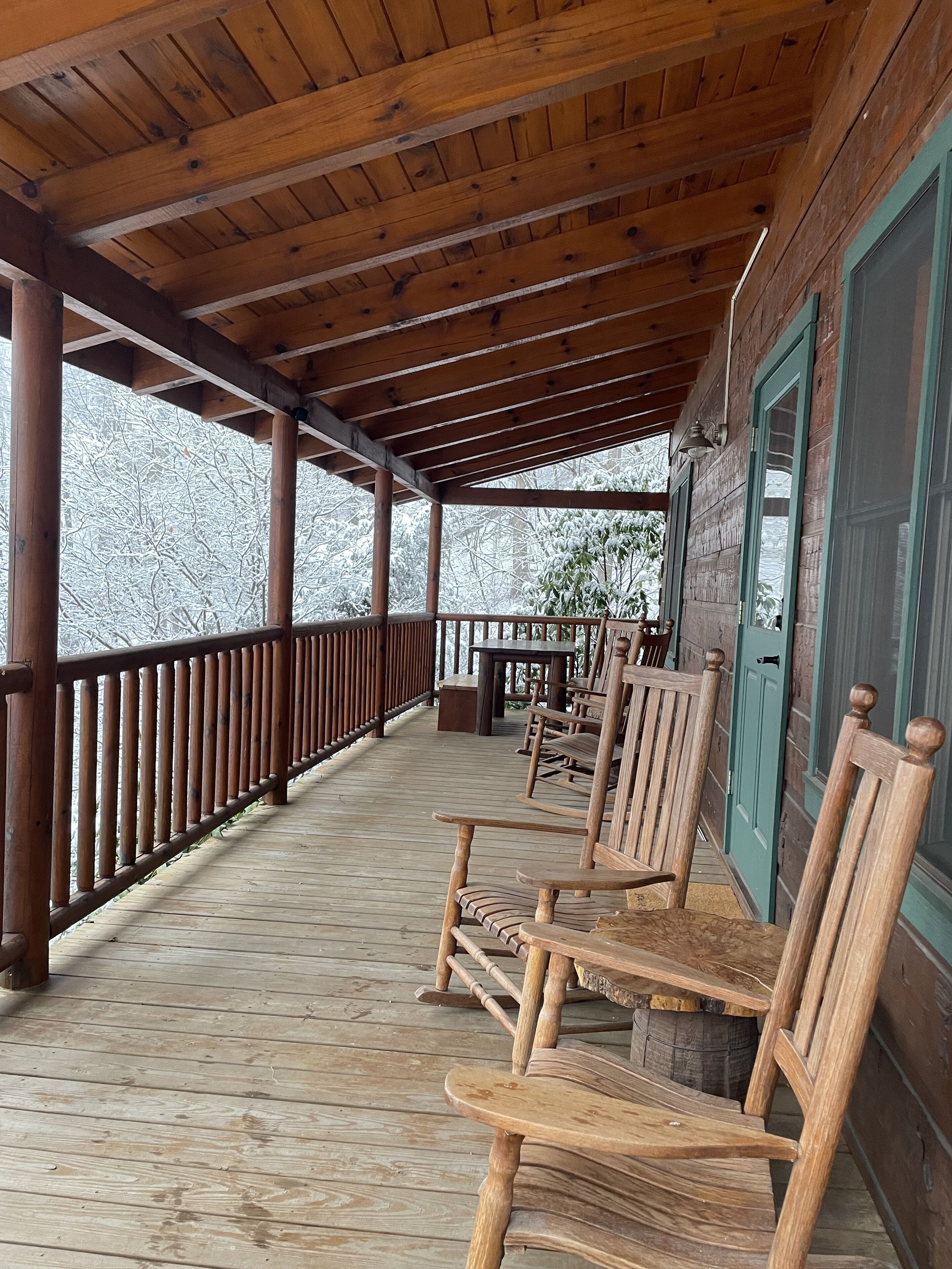 Une véranda en bois avec une balustrade, des fauteuils à bascule en bois et une table.