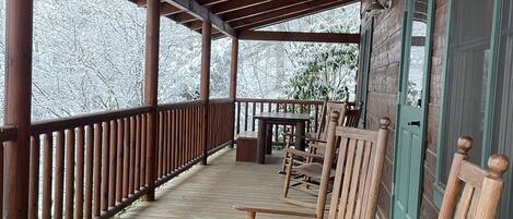 Une véranda en bois avec une balustrade, des fauteuils à bascule en bois et une table.