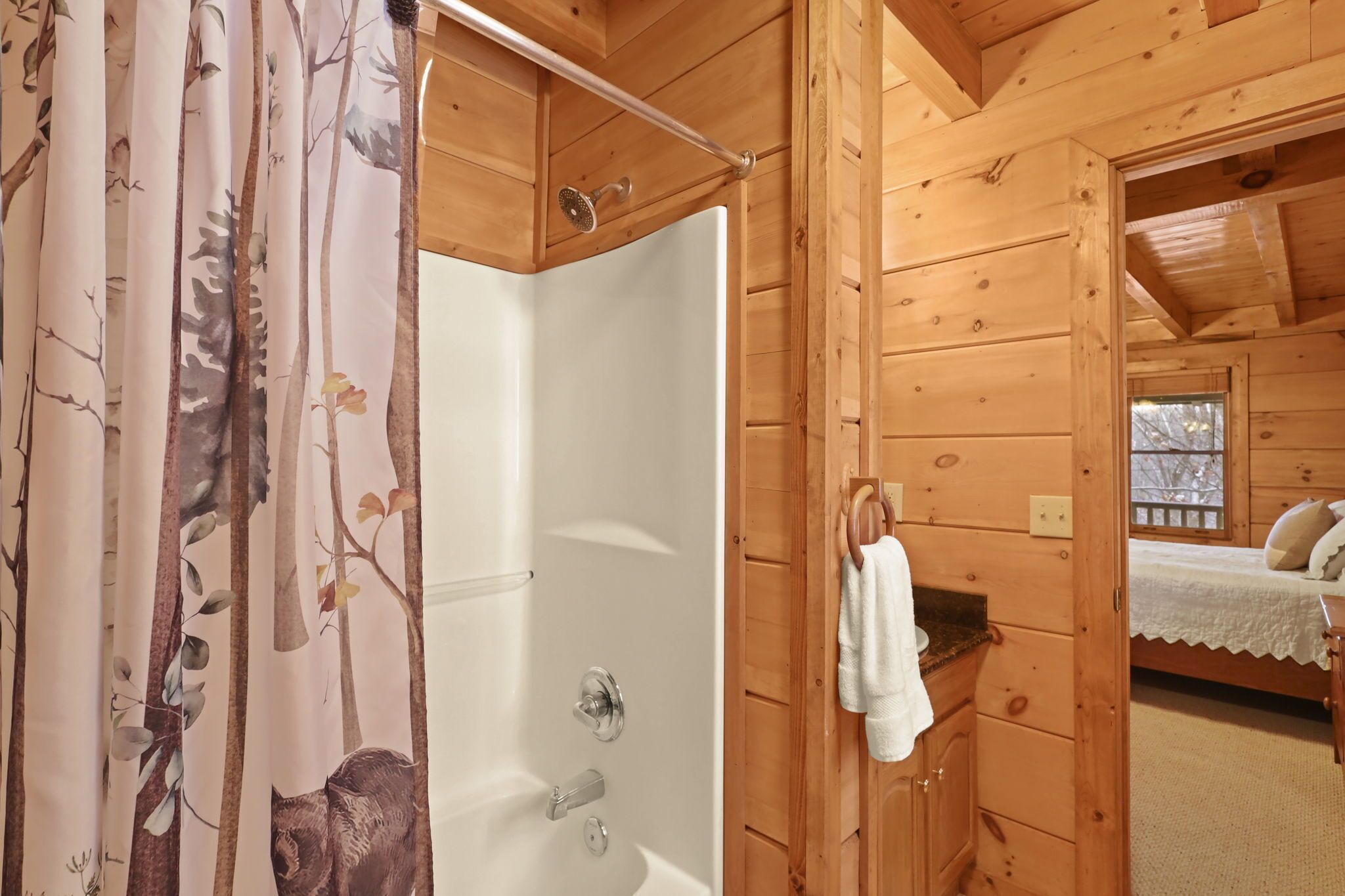 A wooden cabin with a shower area, a bed with a white bedspread, and a towel hanging on a rack.
