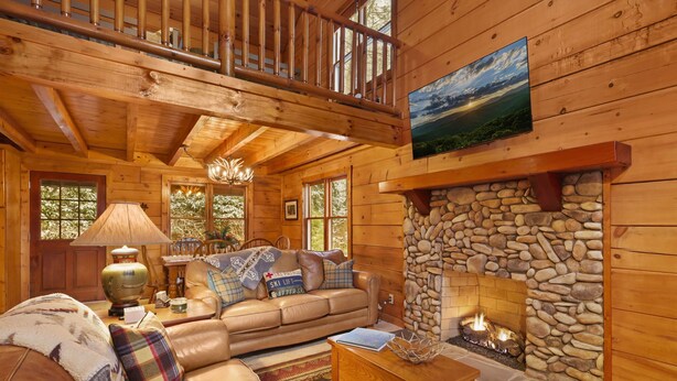 Interior acogedor de una cabaña de madera con chimenea de piedra, sofá de cuero y comedor.