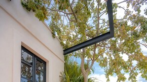 A patio with a sofa and two chairs, a glass door, and a view of trees and a distant building. - Kinal 05 - One Bedroom Apartment, Sleeps 2 (Mérida)
