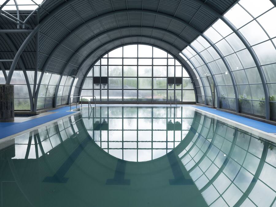 Una piscina interna con tetto in vetro e area bordo piscina azzurra.