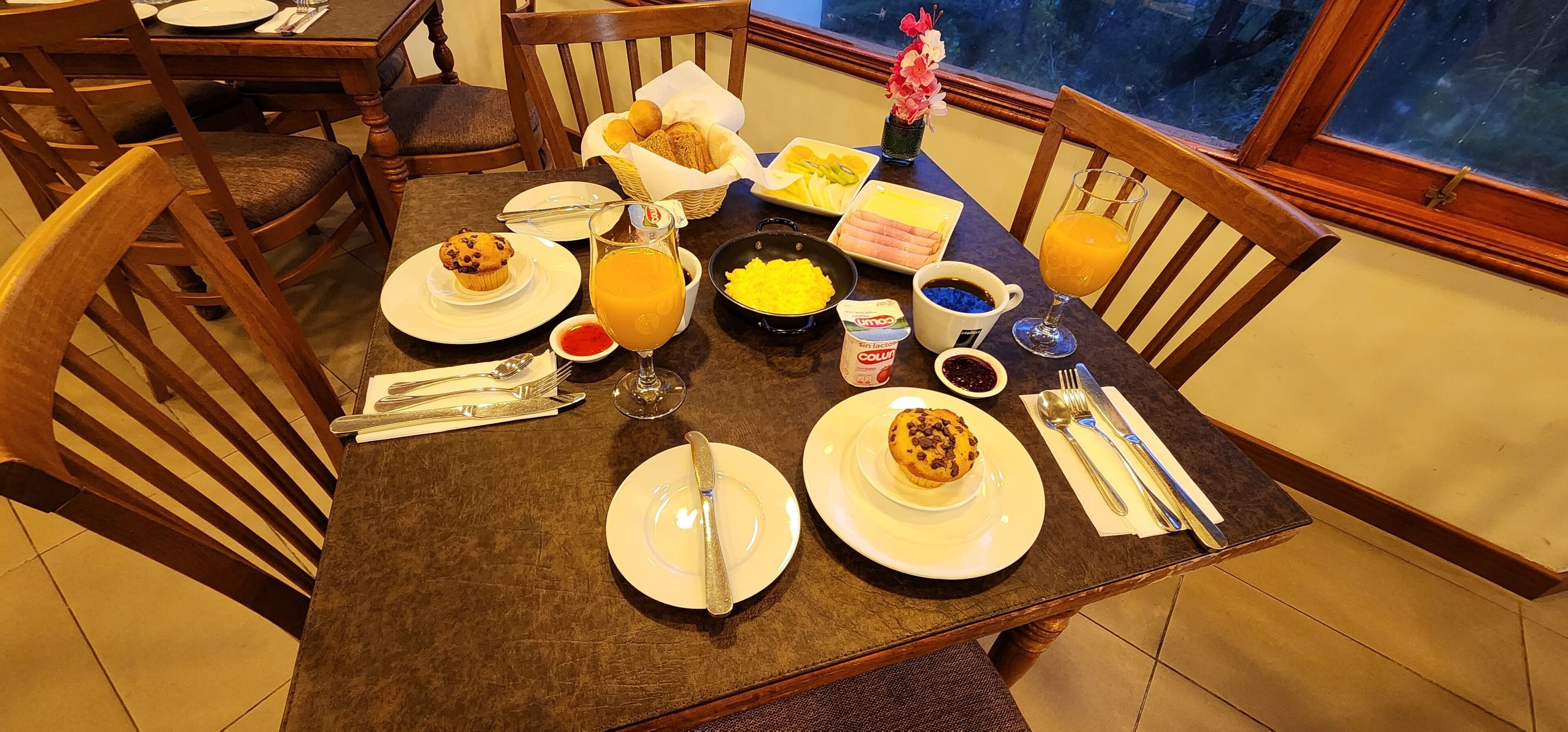 A breakfast setting with plates of food, a glass of orange juice, and a basket of rolls.