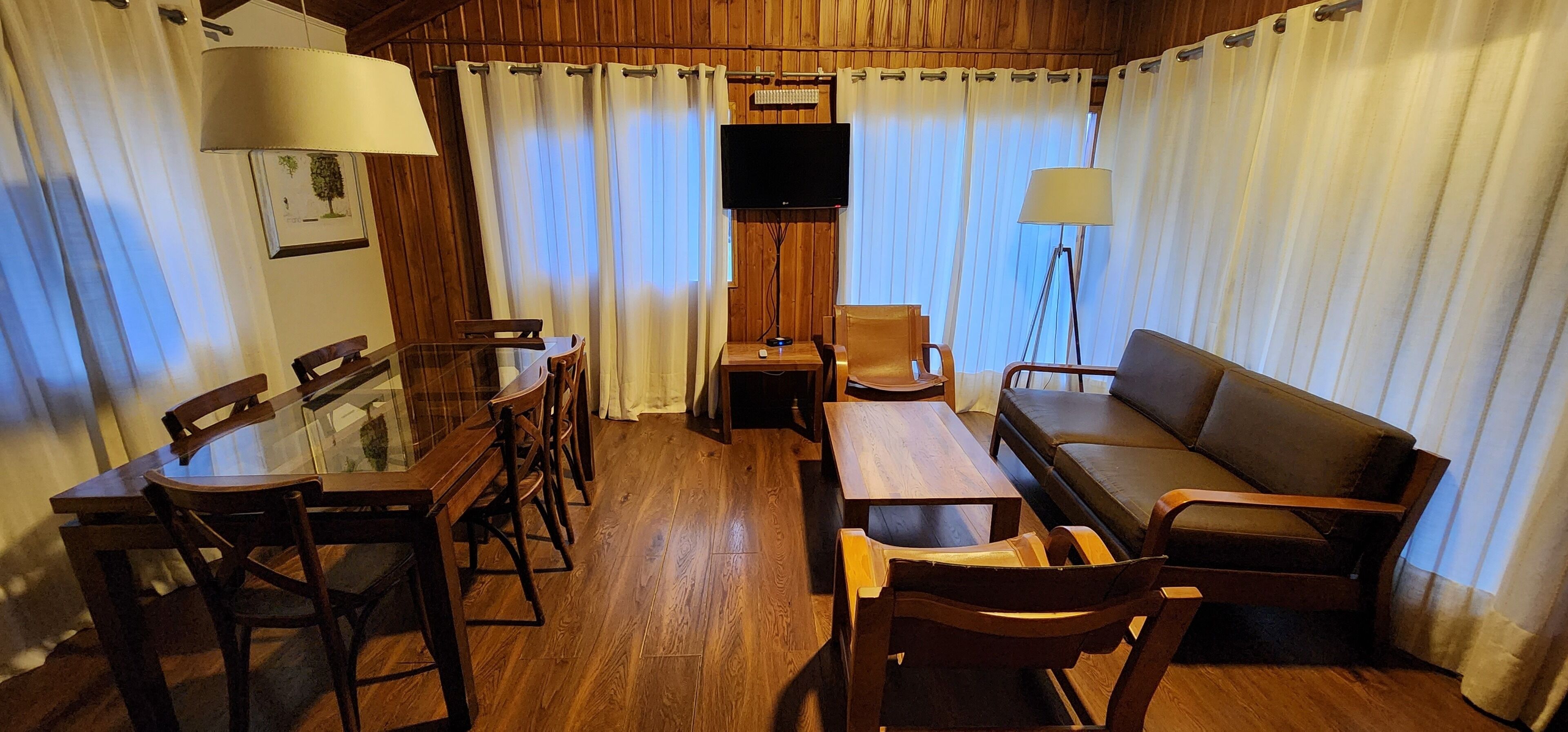 A cozy room with a wooden dining table, chairs, a sofa, and a TV.