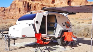 En hvid camper med solpanel, røde klapstole og et kort på jorden.