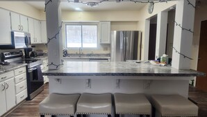 A modern kitchen with white cabinets, stainless steel appliances, a granite countertop, and bar stools.