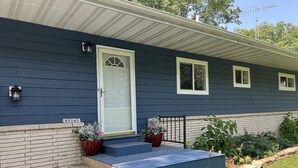 A house with a dark blue exterior, a white door, and a small porch with steps leading up to it. There are two potted plants on the porch.