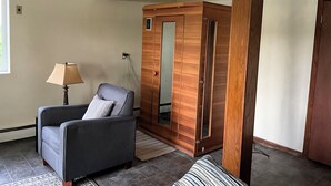 A room with a grey armchair, a wooden wardrobe, and a lamp.