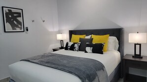 Ein modernes Hotelzimmer mit einem großen Bett, zwei Nachttischen, einem Kopfteil und einem gerahmten Kunstwerk an der Wand.