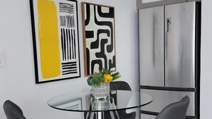 Eine moderne Küche mit Esstisch mit Glasplatte, zwei schwarzen Stühlen, Edelstahlgeräten und abstrakter Wandkunst.
